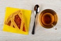 Piece of shortcrust pie with apricot jam on paper napkin, spoon, cup with tea on wooden table. Top view Royalty Free Stock Photo