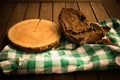 Piece of wood and a bread on a white and green checkered tablecloth on a wooden table Royalty Free Stock Photo