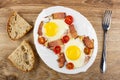 Bread, fried eggs with gammon and cherry tomato in dish, fork on wooden table. Top view