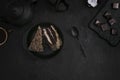 Pieces of cake on a black plate, tea with sweets on a dark background.