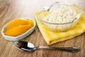 Slices of canned mango in bowl, bowl with cottage cheese on yellow napkin, spoon on wooden table