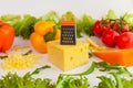 Pieces of cheeses, grated cheese, metal grate, , knife, tomatoes, peppers and leaves of frillis and arugula Royalty Free Stock Photo