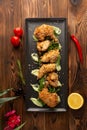 Pieces of chicken in batter on a black plate on a wooden background