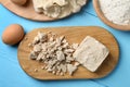 Pieces of compressed yeast, eggs, dough and flour on light blue wooden table, flat lay