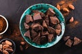 Pieces of dark chocolate in a vintage bowl, cocoa powder and cocoa beans on a dark textured background, top view.