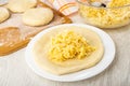 Pieces of dough on cutting board, bowl with mix of cheese and egg, flatbread with cheese in plate on wooden table Royalty Free Stock Photo