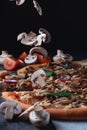 Pieces of flying fall mushrooms on Homemade Italian pizza on a cutting wooden board with ham tomatoes cheese onions and herbs