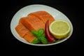 Pieces of Fresh Salmon fillet laying on white plate. isolated on black. Served with chilli pepper, lemon and greens Royalty Free Stock Photo
