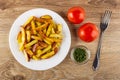 Pieces of fried potato in plate, red tomatoes, bowl with dried parsley, fork on wooden table. Top view Royalty Free Stock Photo