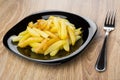 Pieces of fried potatoes in black plate and fork Royalty Free Stock Photo