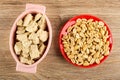 Pieces of halva in pink bowl, fried peanuts in saucer on wooden table. Top view