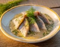 Pieces of herring in mustard sauce with dill. White plate on a wooden table. Outdoor photo.