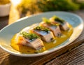 Pieces of herring in mustard sauce with dill. White plate on a wooden table. Outdoor photo.