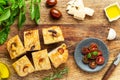 Italian focaccia cut in pieces with garlic cloves and rosemary, alongside a knife, olive oil, parmesan cheese, basil. Royalty Free Stock Photo