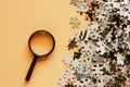 Pieces of jigsaw puzzle with magnifying glass on beige color background Royalty Free Stock Photo