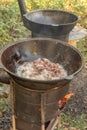 Pieces of meat are fried in hot oil in a cast-iron cauldron on an outdoor wood-burning stove. Royalty Free Stock Photo