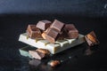 Pieces of milk chocolate with almonds and tiles of white chocolate with hazelnuts on a dark old glossy background
