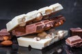 Pieces of milk chocolate with almonds and tiles of white chocolate with hazelnuts on a dark old glossy background