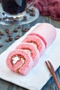 Pieces of pink swiss roll with strawberry jam and cream on a white plate, vertical, closeup