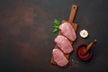 Pieces of raw pork steak with basil, garlic, pepper, salt and spice mortar on cutting board and rusty brown background with space Royalty Free Stock Photo