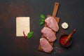 Pieces of raw pork steak with basil, garlic, pepper, salt and spice mortar and piece of paper on cutting board and rusty brown Royalty Free Stock Photo