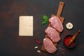 Pieces of raw pork steak with basil, garlic, pepper, salt and spice mortar and piece of paper on cutting board and rusty brown Royalty Free Stock Photo