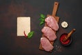 Pieces of raw pork steak with basil, garlic, pepper, salt and spice mortar and piece of paper on cutting board and rusty brown Royalty Free Stock Photo