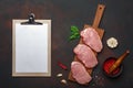 Pieces of raw pork steak with basil, garlic, pepper, salt and spice mortar and tablet on cutting board and rusty brown background Royalty Free Stock Photo