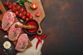 Pieces of raw pork steak on cutting board with cherry tomatoes, rosemary, garlic, pepper, salt and spice mortar on rusty brown Royalty Free Stock Photo