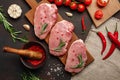 Pieces of raw pork steak on cutting board with cherry tomatoes, rosemary, garlic, pepper, salt and spice mortar on rusty brown Royalty Free Stock Photo