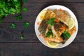 Pieces of roasted carp with lemon and greens on a plate on a dark wooden background Royalty Free Stock Photo