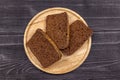Pieces of rye flour black bread on a wooden serving plate and black rustic background