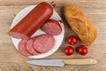 Pieces of sausage in plate, bread, tomatoes and kitchen knife Royalty Free Stock Photo