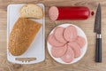 Pieces of sausage in plate, knife, bread on cutting board Royalty Free Stock Photo