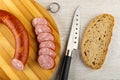 Pieces of sausage, slices of smoked sausage on bamboo cutting board, knife, piece of bread on table. Top view Royalty Free Stock Photo