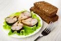 Pieces of smoked mackerel on lettuce in plate, slices of bread, fork on wooden table Royalty Free Stock Photo