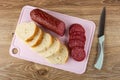 Pieces of sausage, slices of bread on cutting board, knife on wooden table. Top view Royalty Free Stock Photo