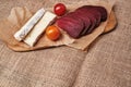 Pieces of soft cheese, dried meat and two cherry tomatoes on parchment paper on the background of a burlap tablecloth. A simple Royalty Free Stock Photo