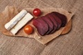 Pieces of soft cheese, dried meat and two cherry tomatoes on parchment paper on the background of a burlap tablecloth. A simple Royalty Free Stock Photo