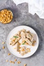 Pieces of sunflower and peanut halva and mint leaves on a plate and a bowl of nuts on the table. Caloric oriental delicacy Royalty Free Stock Photo