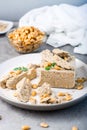 Pieces of sunflower and peanut halva and mint leaves on a plate and a bowl of nuts on the table. Caloric oriental delicacy. Royalty Free Stock Photo