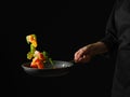 Pieces of trout with pieces of vegetables and herbs in a frying pan. Levitation. A chef in a black uniform holds a frying pan in