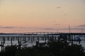 Pier, boats and bridge in silhouette against a pink sky as sunset.