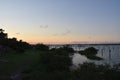 Pier, boats and bridge in silhouette against a pink sky as sunset.