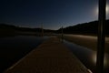 Pier extending over a lake on a clear night with the full moon and stars illuminating the beach Royalty Free Stock Photo