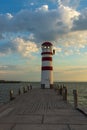 A pier leading to the lake and a red and white lighthouse on Lake Neusiedl in Podersdorf, Austria. In the background is a dramatic Royalty Free Stock Photo