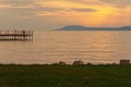 Pier with many birds at the Lake Balaton during sunset. Sun reflected in the water, mountain at the background