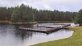 A pier with metal railings is built on the water near the lake shore. There are reeds in the water. On the water ripples. On the o Royalty Free Stock Photo