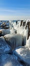 Pier poles and rocks covered with snow on a sunny winter day with some sun rays shining on them and the sea in the Royalty Free Stock Photo