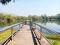 The pier in public park with danger warning sign. Silver handrail with wooden walkway near the lake with landscape view